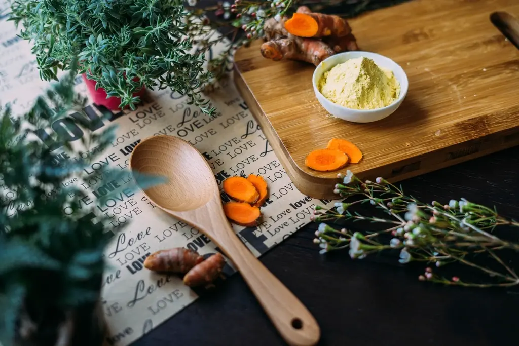 Fresh turmeric root and a wooden spoon on a kitchen counter.