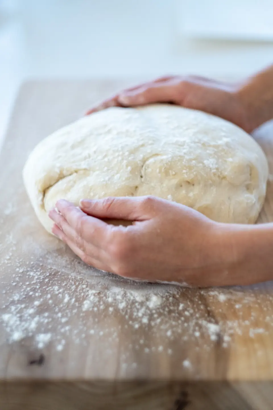 Hands kneading dough on a floured counter.