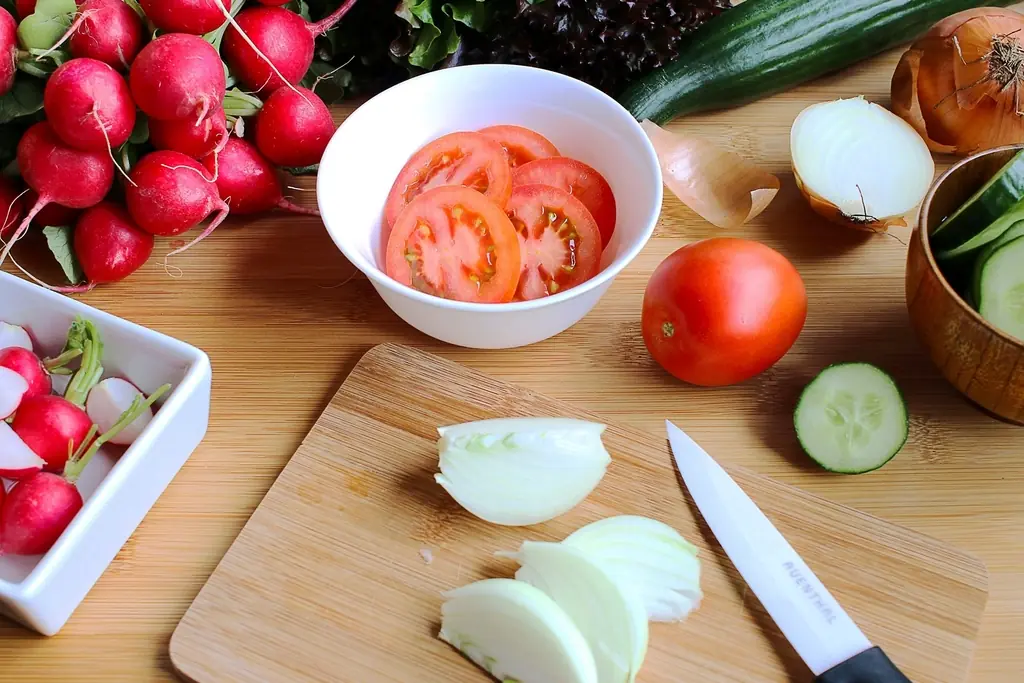 Tomatoes, onion and cucumber being prepared on a wooden board.